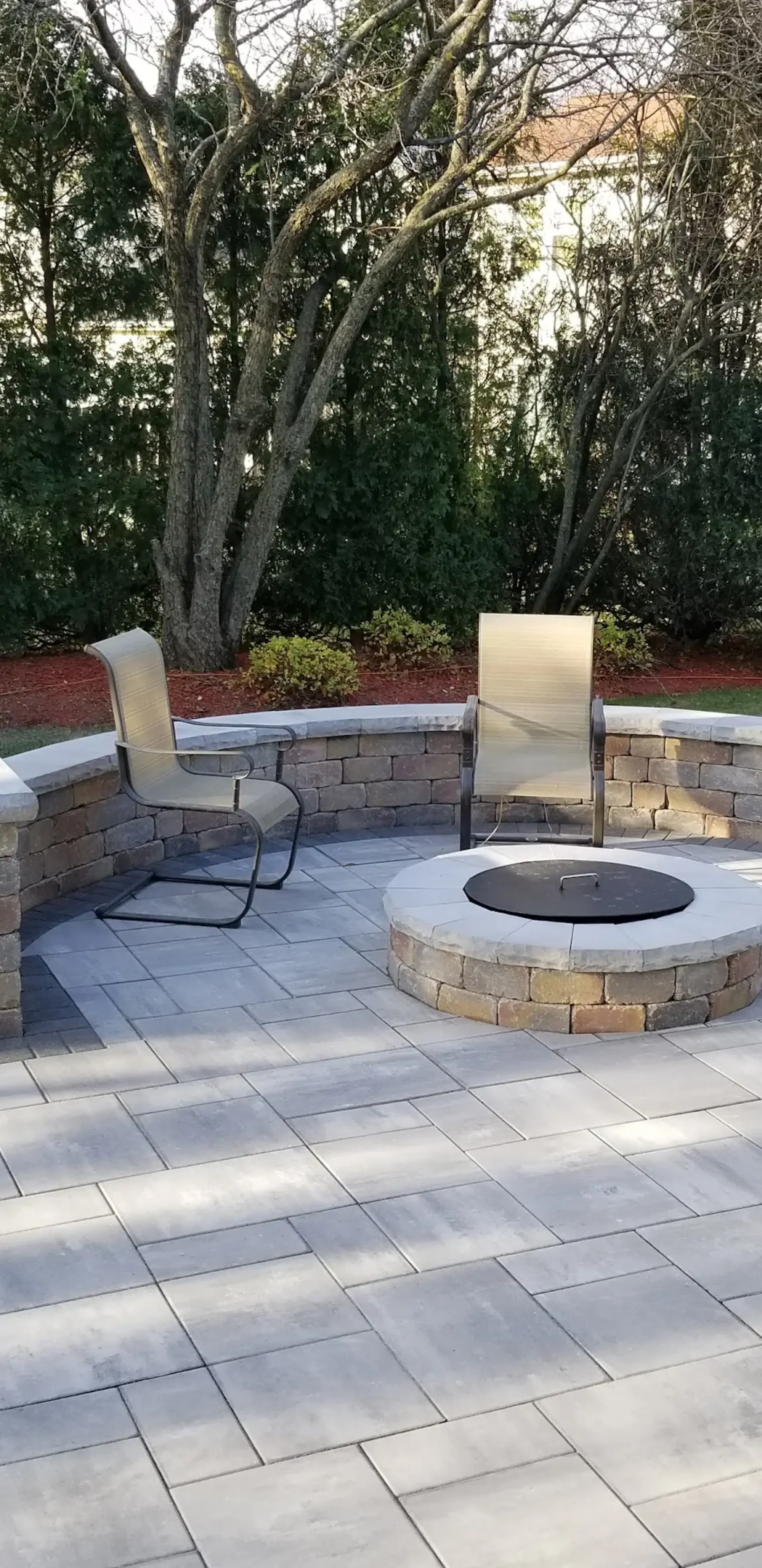 Circular Unilock paver patio with stone fire pit and wicker chairs
